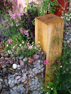 a wooden block sitting next to a garden filled with flowers and rocks in front of a fence