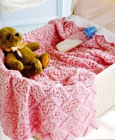 a brown teddy bear sitting in a pink crocheted blanket