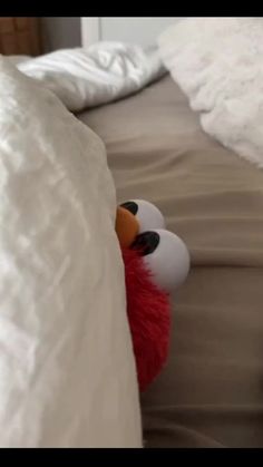 a red stuffed animal peeking out from behind the covers on a bed with white sheets