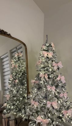 a white christmas tree with pink bows on it in front of a mirror and other decorations