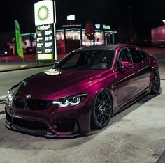 a purple car is parked in front of a gas station at night with its lights on