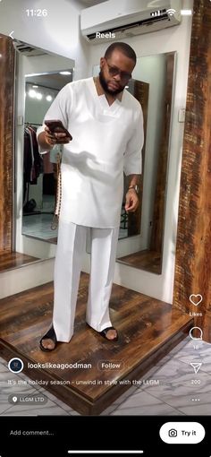 a man standing in front of a mirror looking at his cell phone while wearing a white outfit