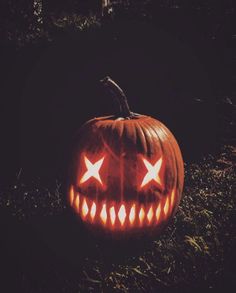 a carved pumpkin sitting in the grass with glowing eyes