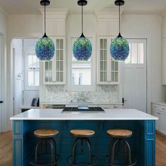 three lights hanging from the ceiling above a kitchen island with stools in front of it