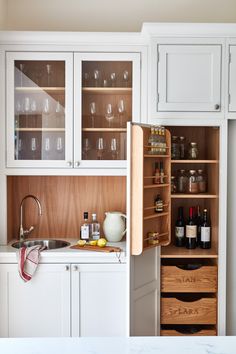 a kitchen with white cabinets and wine glasses in the cupboards next to the sink