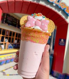 a person holding up an ice cream sundae in front of a building with hello kitty decorations on it