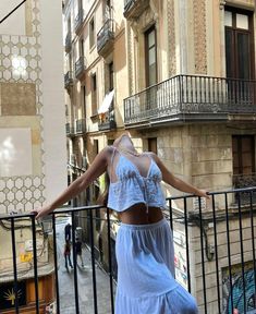 a woman in a blue dress is standing on a balcony looking down at the street