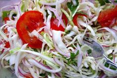 a salad with red onions, tomatoes and lettuce on a glass plate next to a fork