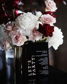 a vase filled with white and red flowers on top of a wooden table next to a black sign