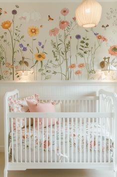 a white crib in front of a floral wallpaper with lights on the headboard