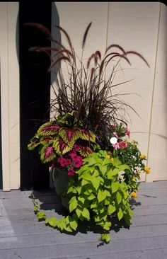 a planter filled with lots of flowers sitting on top of a wooden floor next to a building