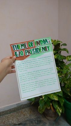 a person holding up a sign in front of a potted plant