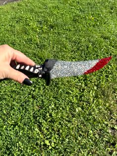 a hand holding a black and red knife on top of green grass in a field