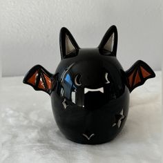 a black cat helmet with orange eyes and bats on it's face is sitting on a white surface