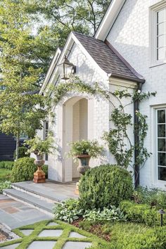 an instagram photo of a white house with plants on the front porch and steps leading up to it