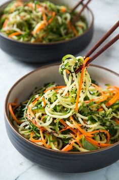 two bowls filled with vegetables and chopsticks on top of a marble countertop