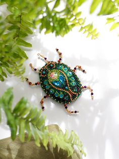 a beaded brooch sitting on top of a green leafy plant next to a white wall