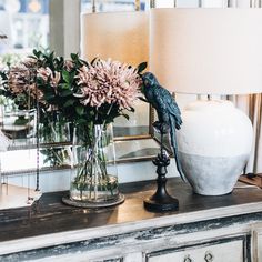 a vase with flowers and a lamp on a table in front of a mirror that is next to a dresser