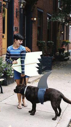 a woman is walking her dog on the sidewalk with a surfboard in his mouth