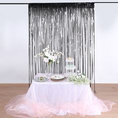 a white table topped with cake and cupcakes next to a black wall hanging from the ceiling