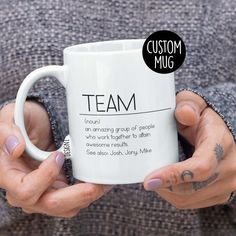 a person holding a white coffee mug with the words team on it and a black circle sticker