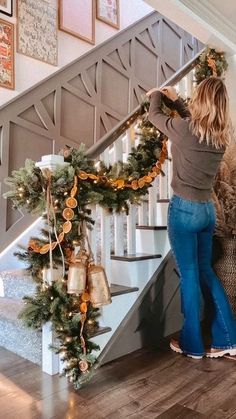 a woman is standing on the stairs decorated with garlands and christmas lights as she puts decorations on the banister