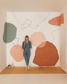 a woman is sitting on the floor in front of a wall with abstract shapes painted on it