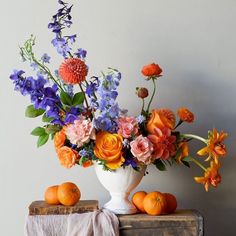 a white vase filled with lots of flowers and oranges on top of a table