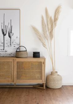 a wooden cabinet sitting next to a wall with plants on top of it and a painting behind it