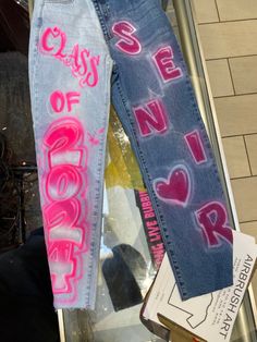 two pairs of jeans with writing on them sitting next to each other in front of a store window