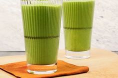 two glasses filled with green smoothie on top of a wooden table