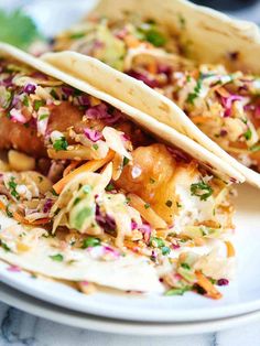 two tacos are sitting on a plate with coleslaw and other toppings