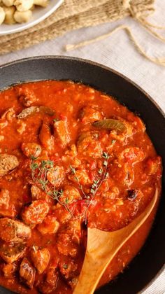 a skillet filled with meat and sauce on top of a table next to potatoes