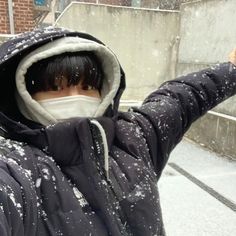 a man wearing a face mask while standing in the snow with his hand up to the camera