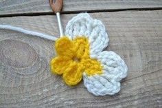 a crocheted flower with yellow and white petals on a wooden surface next to a knitting hook