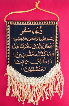 an arabic calligraphy hanging on a pink wall with tassels and beads around it