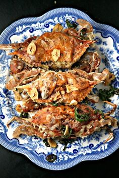 three cooked crabs are on a blue and white plate with spinach sprouts