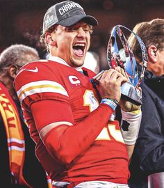 a man holding a trophy in his right hand and yelling at the camera with other people behind him