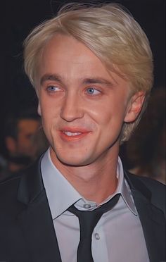 a close up of a person wearing a suit and tie with blonde hair smiling at the camera