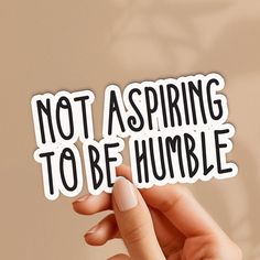 someone holding up a sticker that says not aspring to be humble