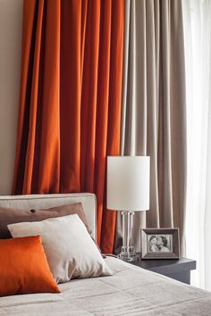 a bedroom with orange drapes and a bed in front of a window filled with pillows