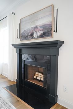 a fireplace in a living room with a painting on the wall and hardwood flooring