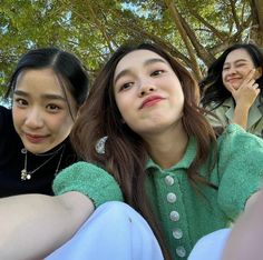 three young women sitting next to each other on the ground with trees in the background