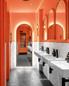 an orange bathroom with sinks and mirrors on the walls is lit up by lights above them