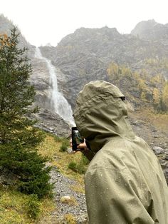 a man in rain gear taking pictures of a waterfall from the side of a mountain