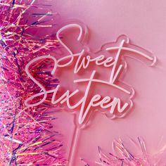 a pink neon sign that says sweet sixteen on it next to some tinsel and confetti