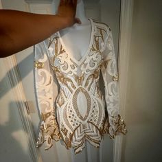 a white and gold dress is being held up by someone's hand in front of a door