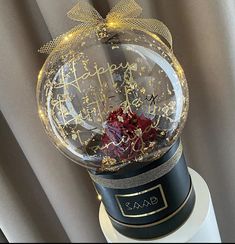 a snow globe with red roses in it on top of a white stand next to a curtain