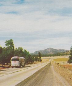 the bus is driving down the road in the middle of the desert, with mountains in the background