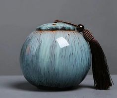 a blue vase with a tasseled lid on a gray surface, against a grey background